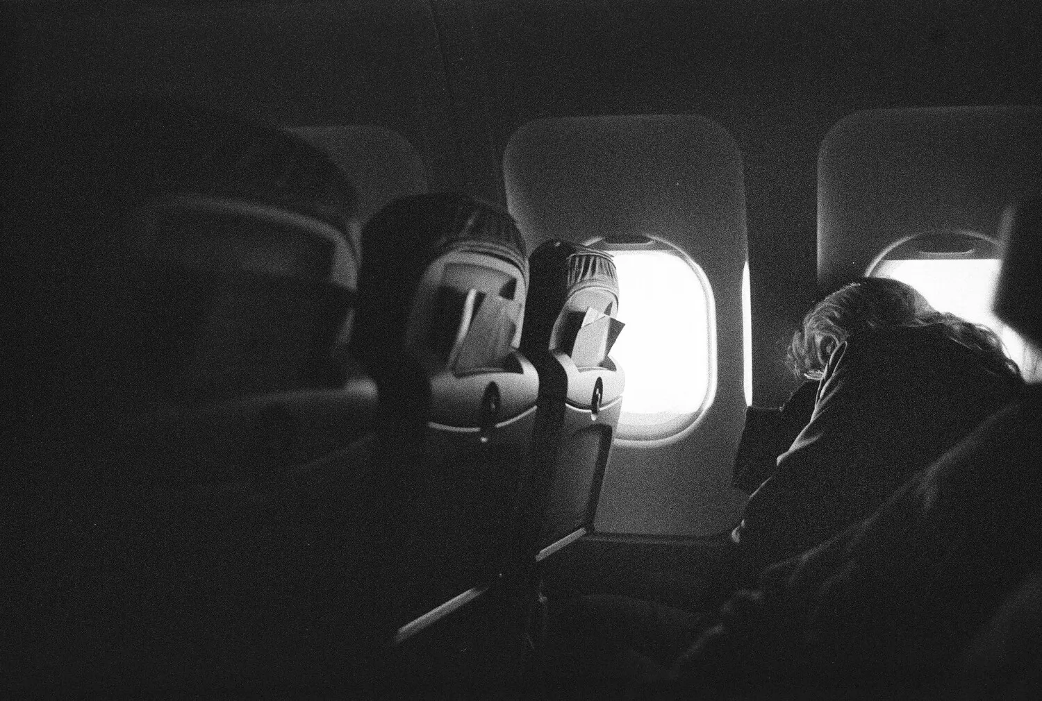 A black and white photograph of an airplane cabin with light streaming through the windows.