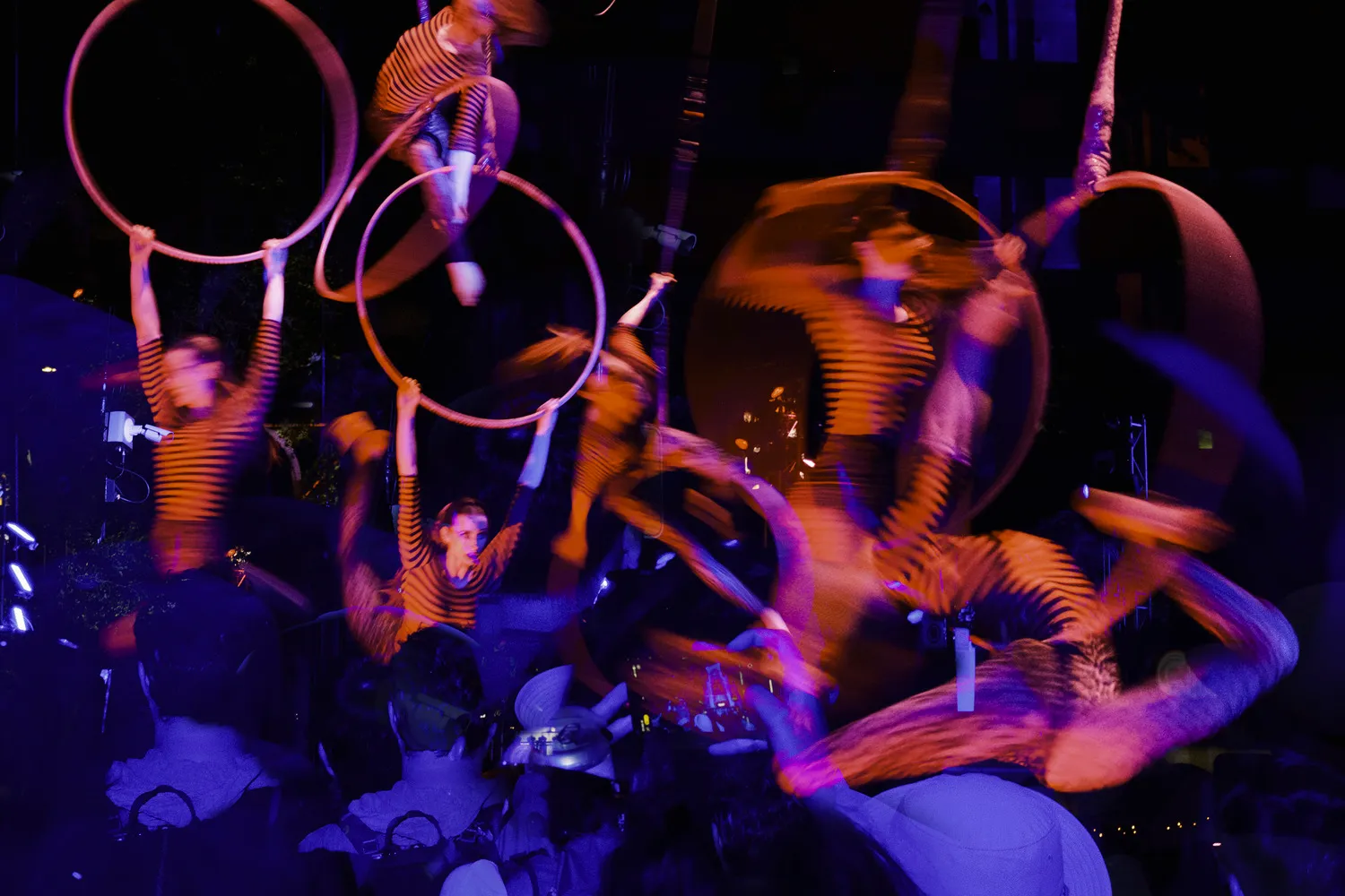 A multiple-exposure photo of acrobats performing with glowing hoops on a dark stage.