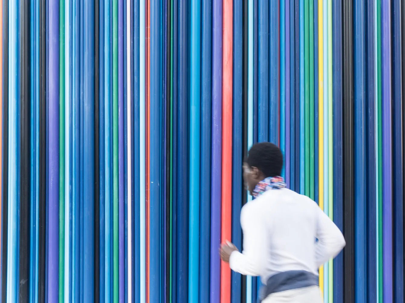 A person running past a vibrant installation of colorful vertical poles.