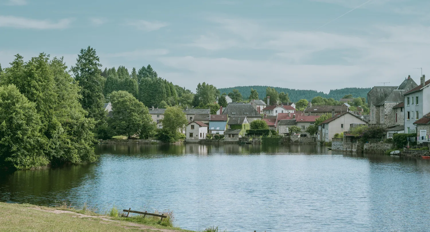 A peaceful French village nestled along the edge of a calm lake surrounded by trees.