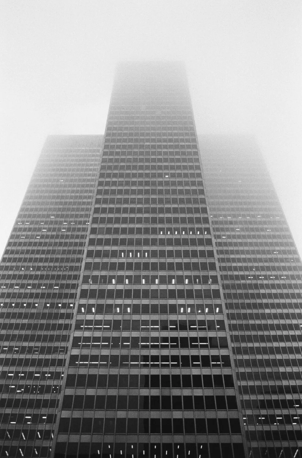 A low-angle black and white photograph of a tall skyscraper disappearing into thick fog.
